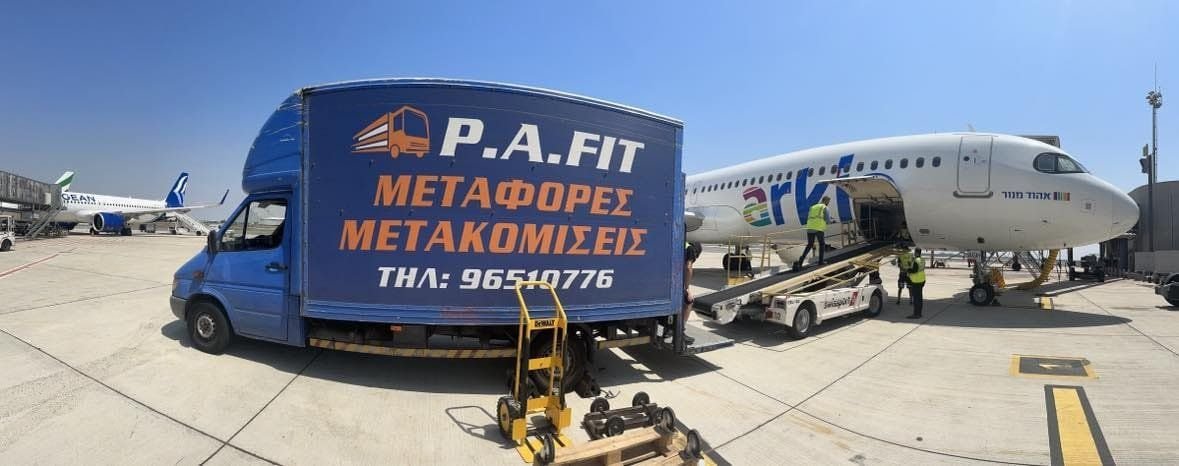 P.A.FIT moving truck parked on an airport apron beside a passenger jet, with hand trucks and dollies ready for loading